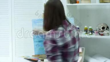 一个年轻的女人在画布上画一幅画，站在画架后面，在一个<strong>大气</strong>的车间里。 时间唇